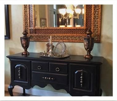 A black sideboard beneath an ornate mirror